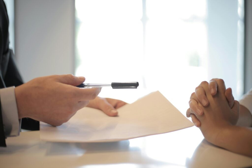 Person handing pen to another over document.