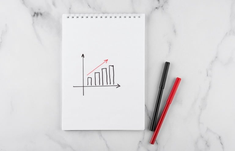 Notebook with graph and pens on marble surface.