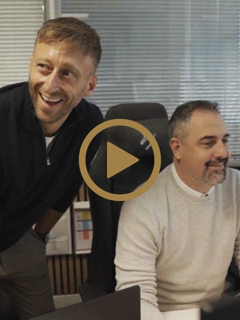Two men smiling while working at computer desks.