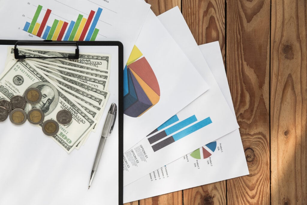 Financial documents, graphs, and currency on wooden table.