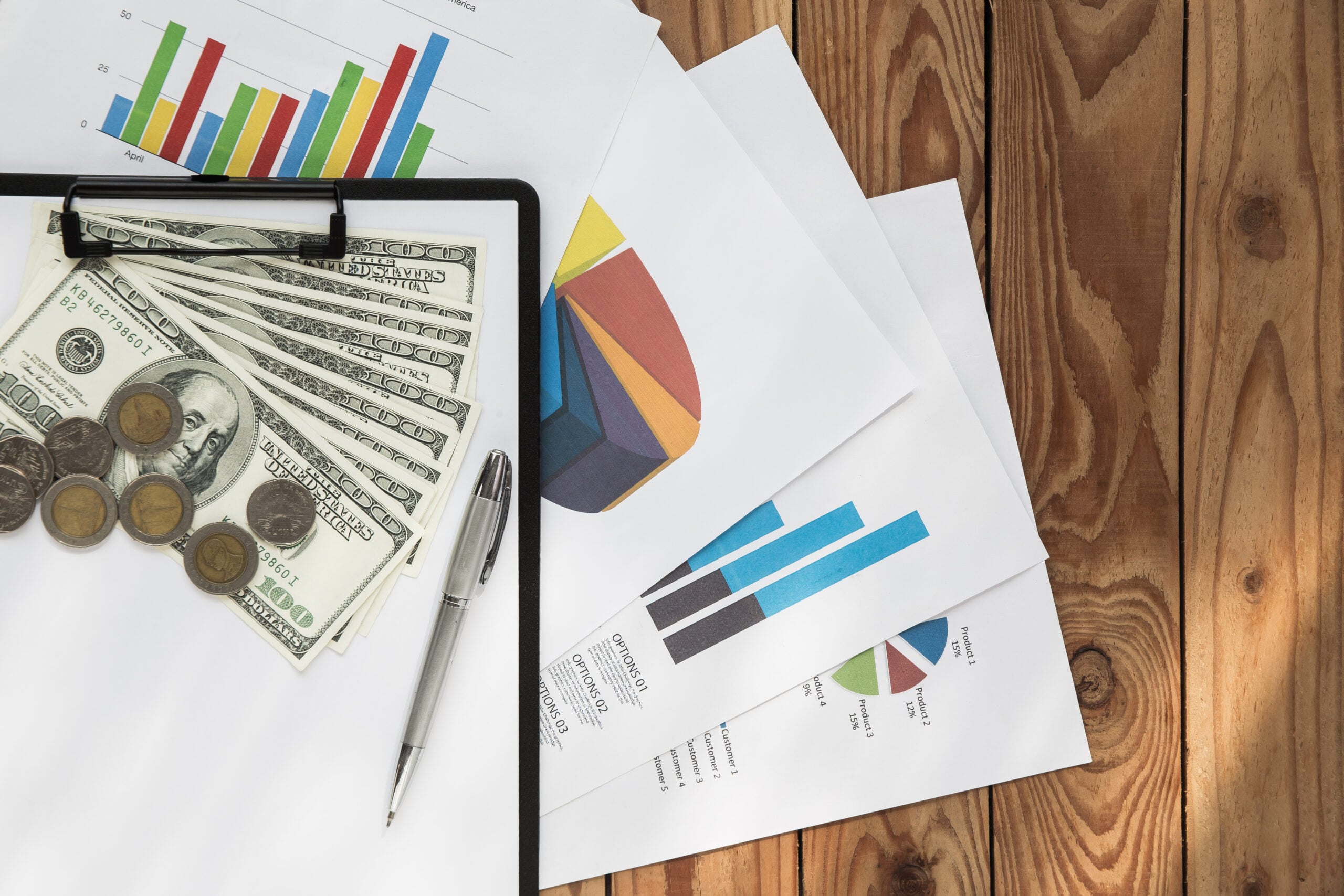 Financial documents, graphs, and currency on wooden table.