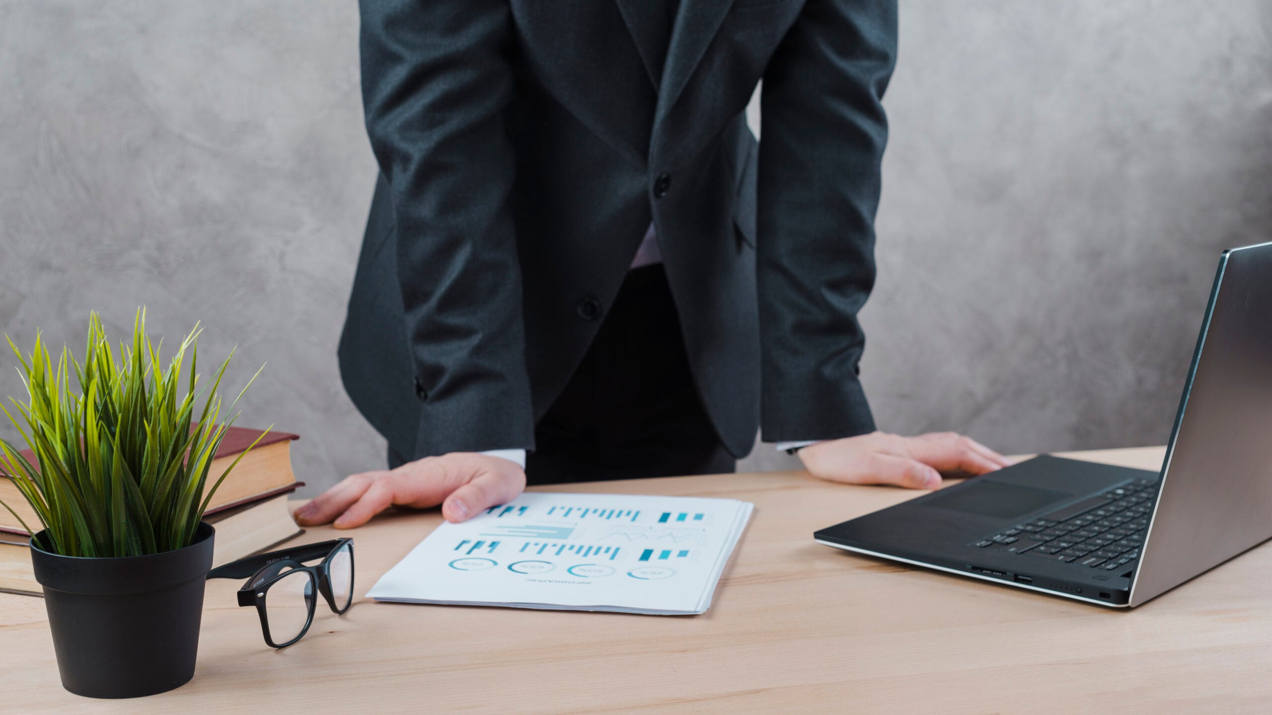 Person analysing business reports on desk with laptop.