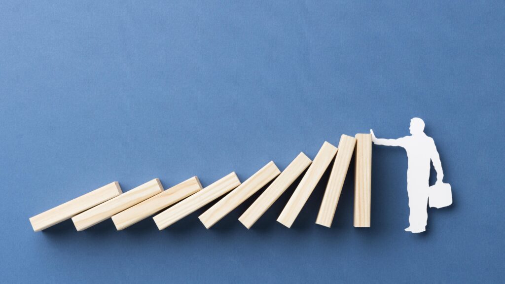 Silhouette stopping falling dominoes on blue background.