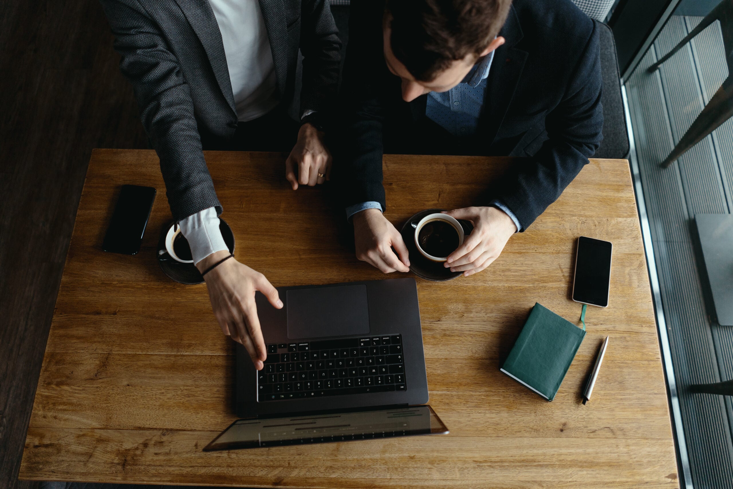 Two people collaborating at a wooden table with laptop.